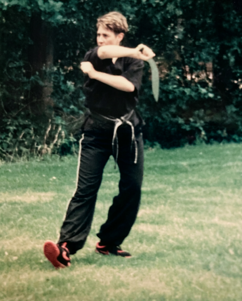 Vintage photo of young martial artist practicing stance and strike outdoors in black uniform