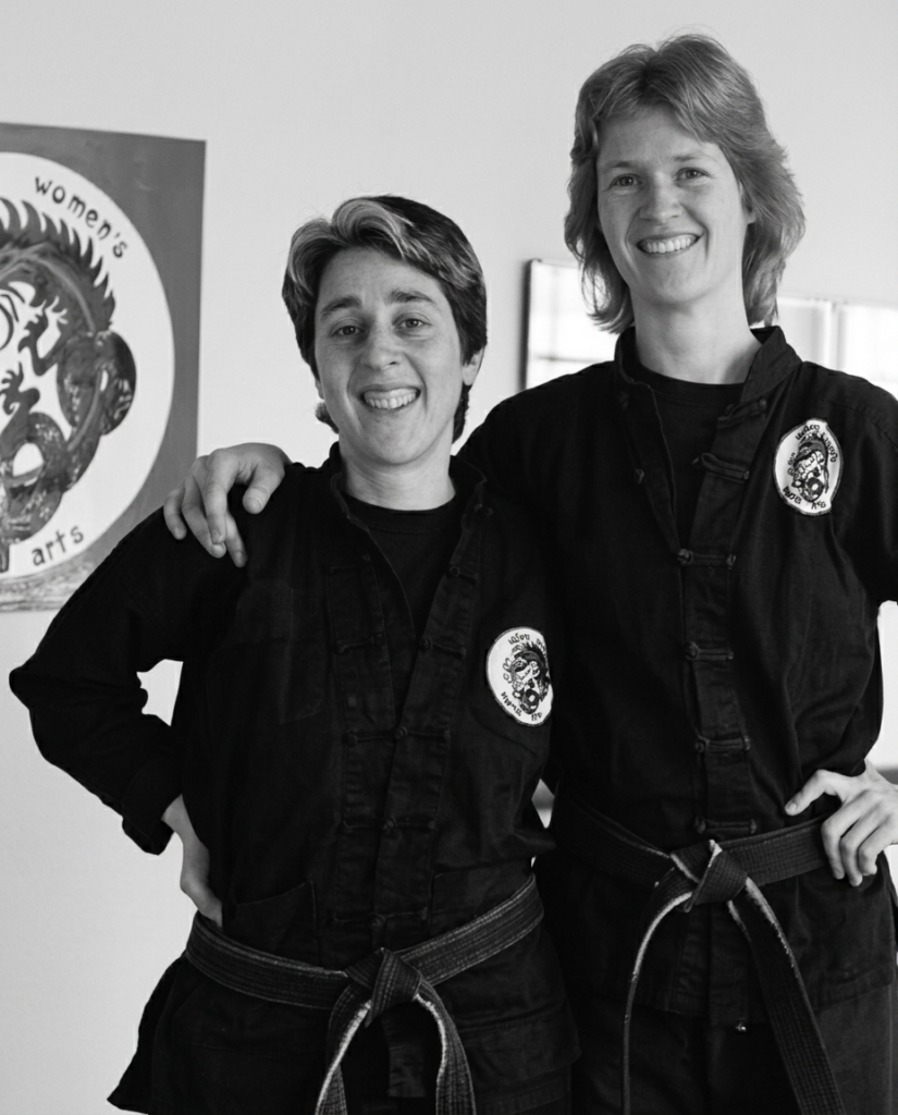 Archival photo of two black belt martial artists smiling, Women's Martial Arts patch on uniforms